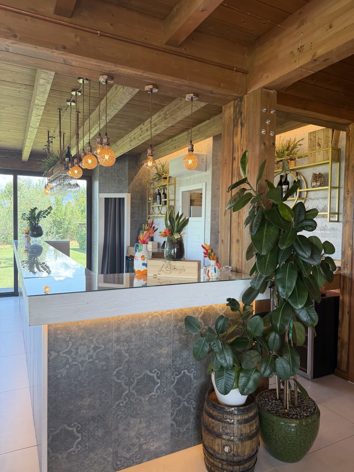 The bar and reception under an exposed timber roof, filament pendant lights above the counter and a rubber plant in a barrel
