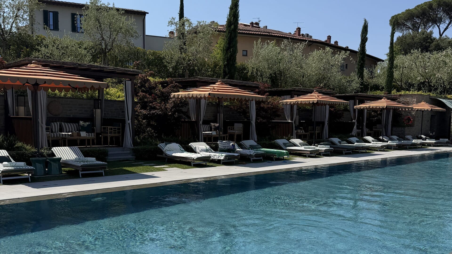 The main pool at Collegio alla Querce, lined with cabanas and orange umbrellas