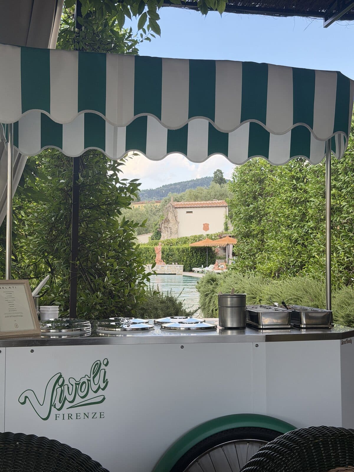Vivoli gelato cart under a striped awning with the pool framed behind