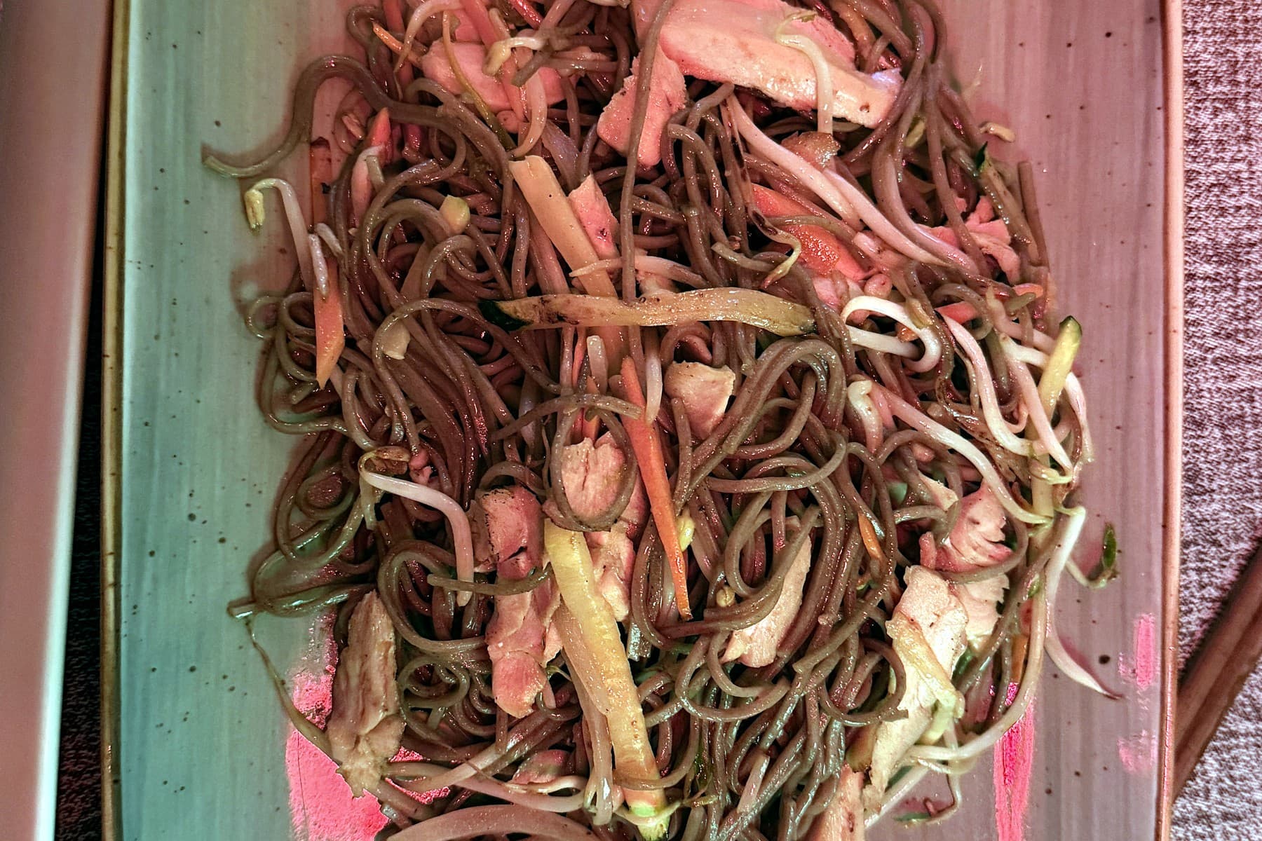 A plate of peanut chicken yaki soba, noodles with chicken and vegetables, under heavy red light