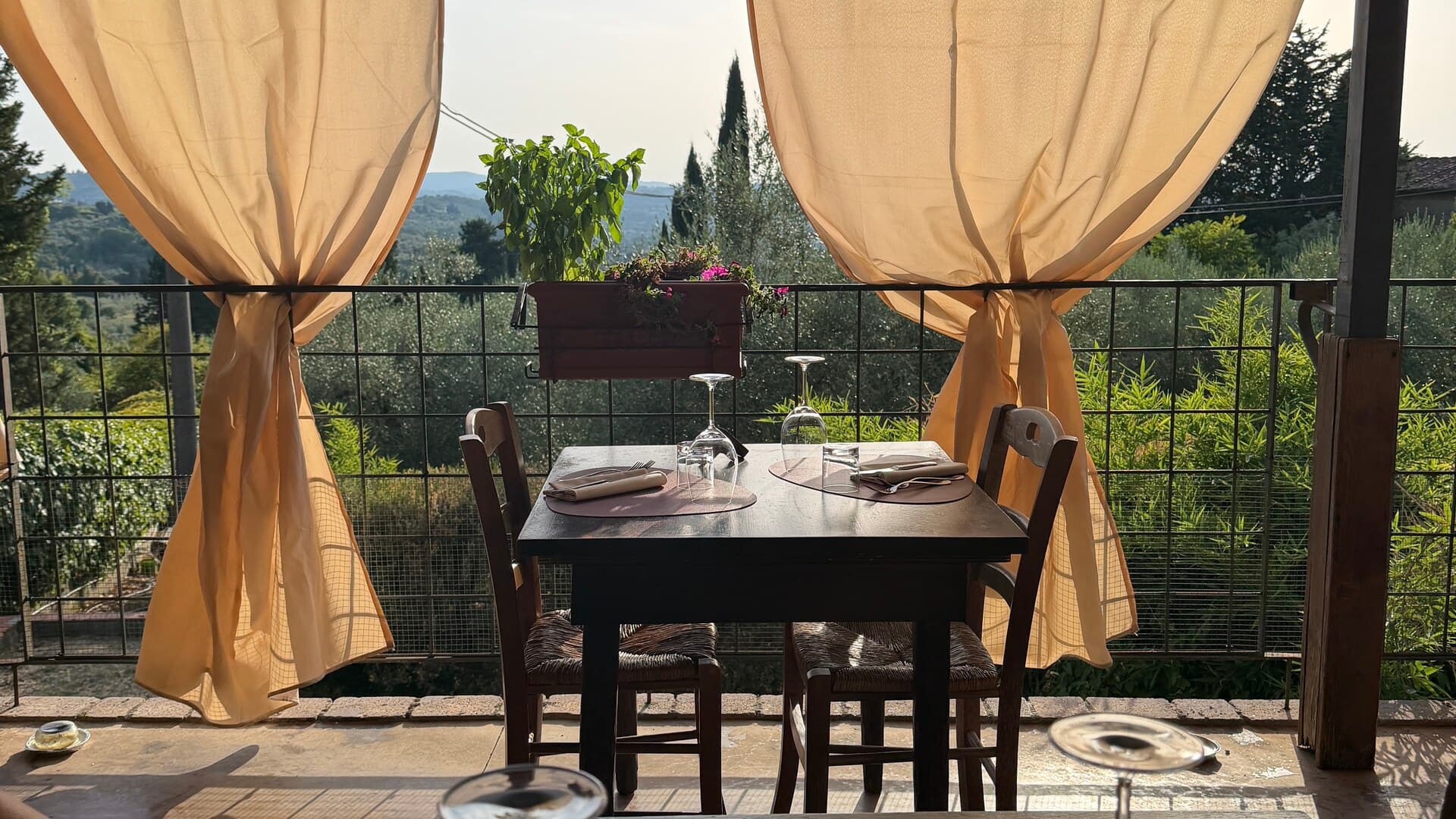 A set table on the terrace at Trattoria La Gargotta, curtains tied back, Tuscan hills beyond