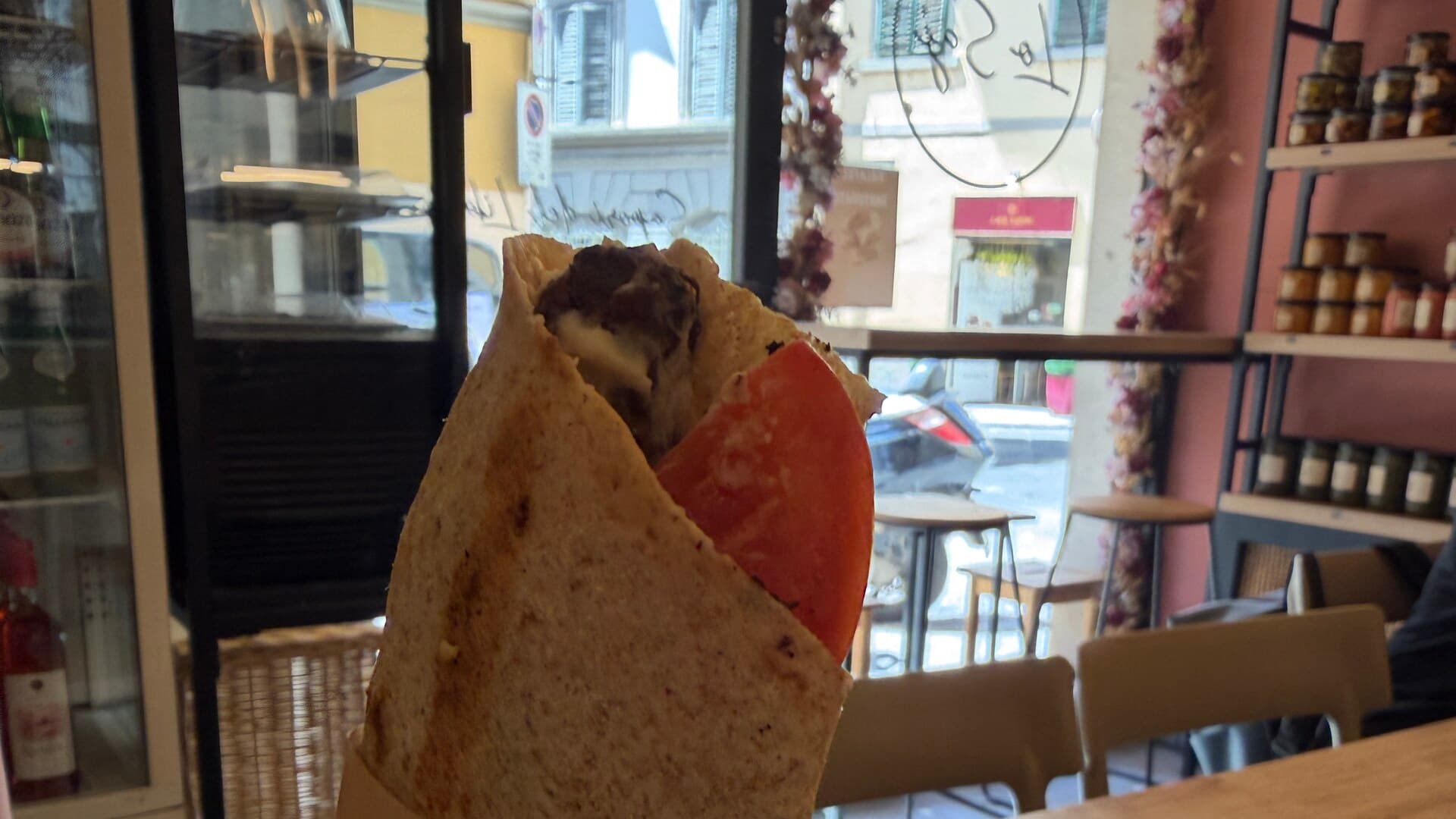 A kafta and hummus wrap held up inside Lo Saj, with the San Lorenzo street behind