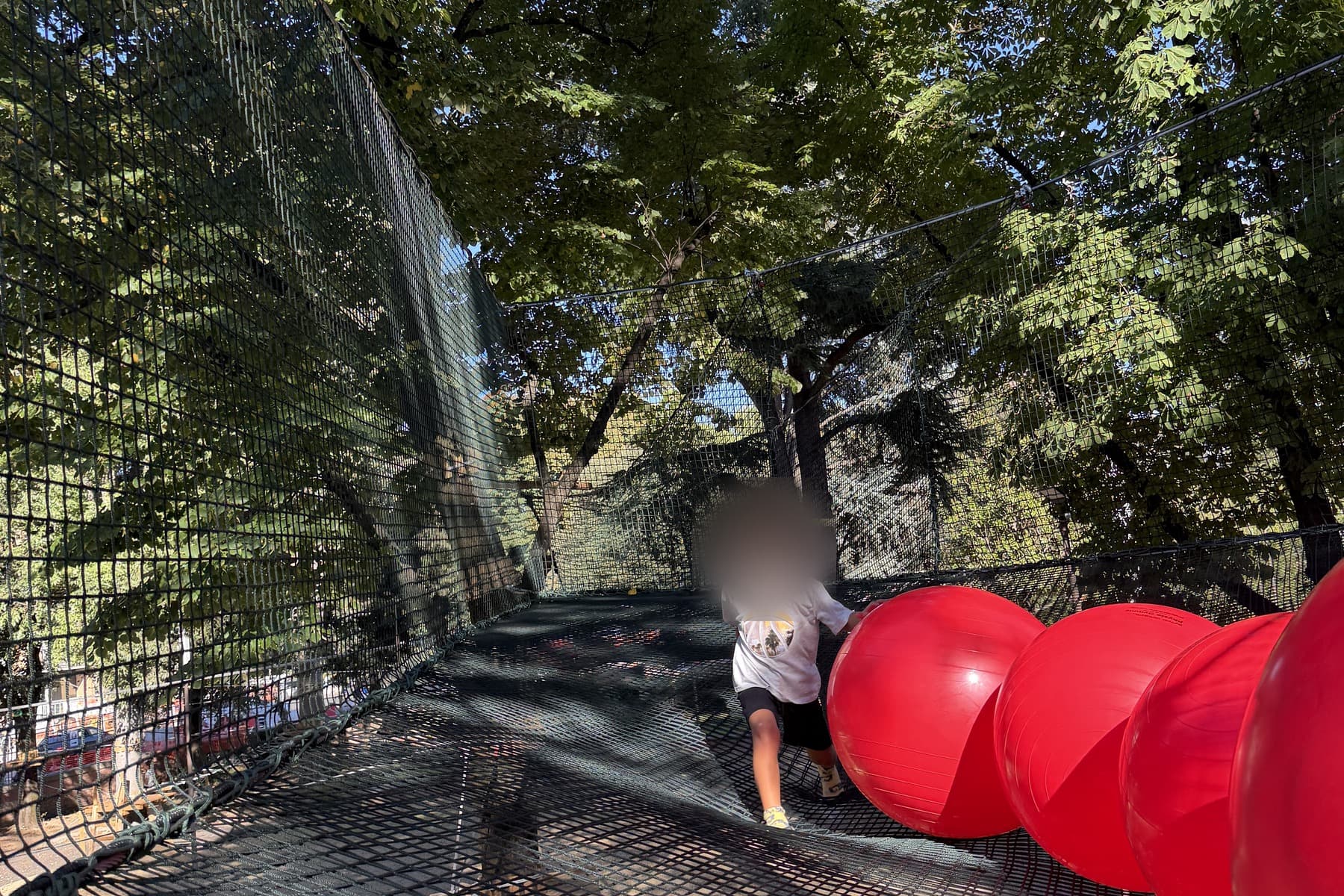 A child walking across the suspended net beside a row of giant red balls