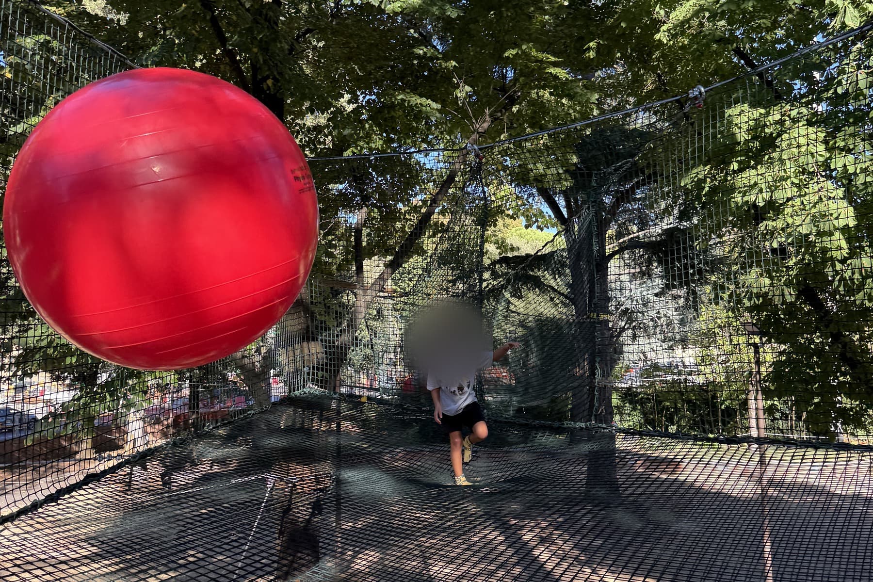 A giant red ball hanging in the netting with a child beyond it