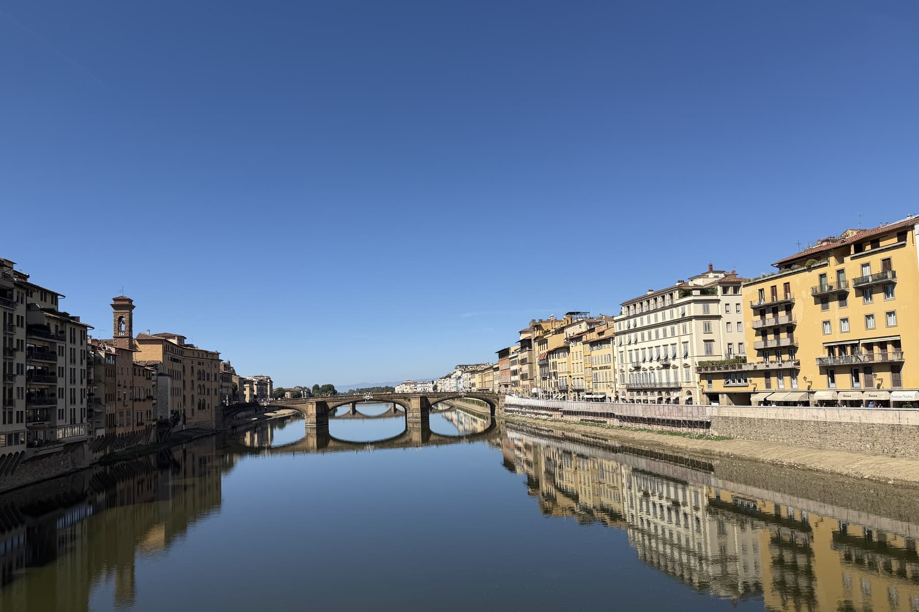 The Arno still and reflecting the Lungarno buildings under clear September sky