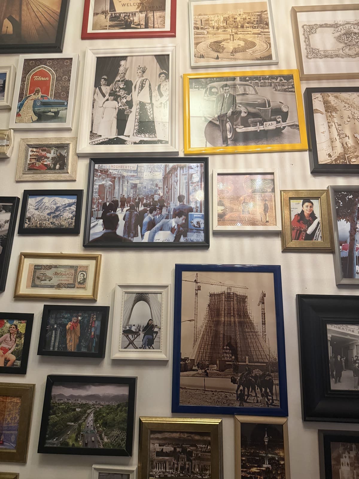 A wall of framed photographs of Iran, Tehran street scenes and the Azadi Tower among them