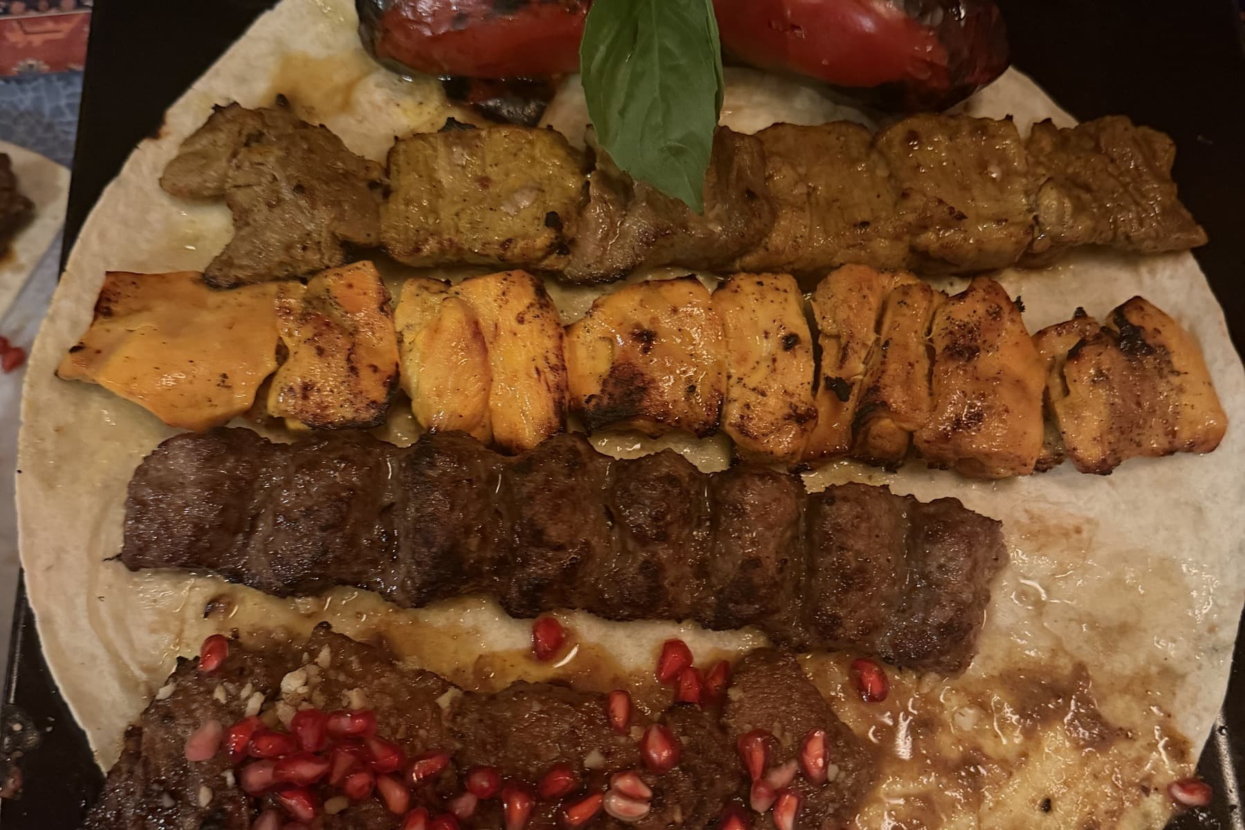 Four kebab skewers on flatbread, minced meat, saffron chicken and pomegranate-marinated fillet, with grilled tomato and basil