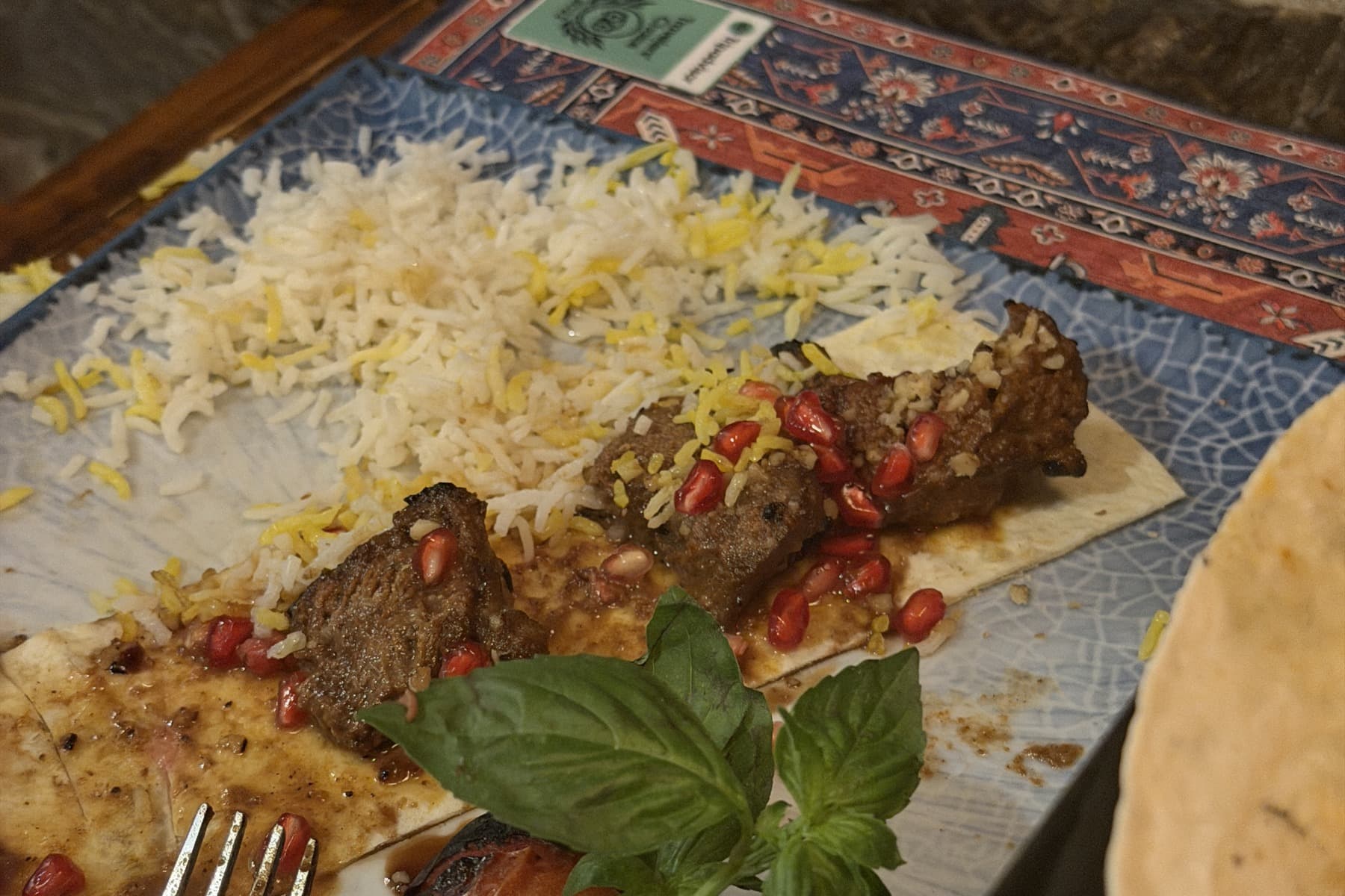 Pomegranate-marinated beef fillet on saffron rice with pomegranate seeds and basil, on a Persian-patterned cloth