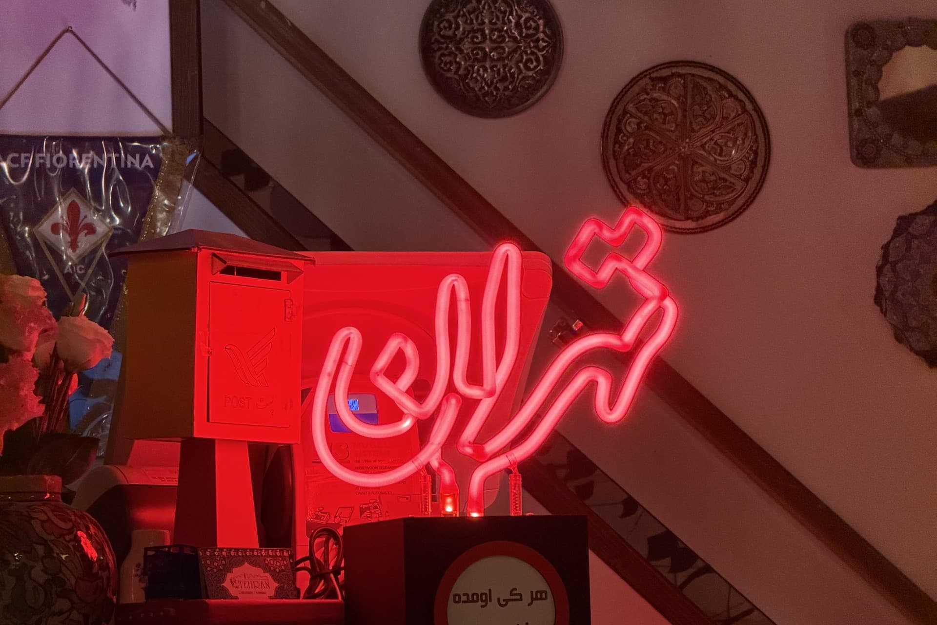 The red neon sign reading Tehran in Persian script above the bar, with a Fiorentina pennant and a small round sign below it
